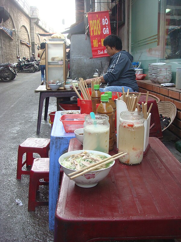 A pavement phở stall in Hanoi, with low stools and jars of pickled garlic